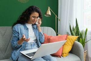 en línea consulta con un psicólogo, latín americano mujer a hogar sentado en el sofá llorando utilizando un ordenador portátil para un vídeo llamada y consulta con un doctor, Deprimido mujer en el vivo habitación foto