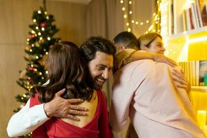 Diverse friends congratulate each other on New Year, hug for Christmas at home near the Christmas tree in the living room. photo