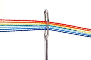 multi-colored threads for sewing in the form of a rainbow pass through an antique needle on a white background photo