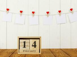 blanco piezas de papel en pinzas para la ropa con un corazón en un de madera fondo, calendario febrero 14 foto