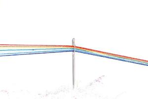 multi-colored threads for sewing in the form of a rainbow pass through an antique needle on a white background photo