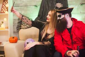 Vampire woman taking a selfie with smiling pirate at halloween celebration. photo