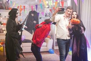 Male zombie taking a selfie with woman witch holding a pumpkin at halloween celebration. photo