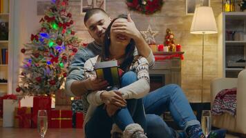 Husband covering his wife eyes to give her a surprise gift on christmas day. Champagne glasses. photo