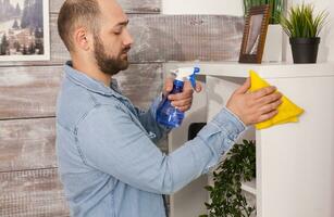 Man dusting the furniture in his apartment photo