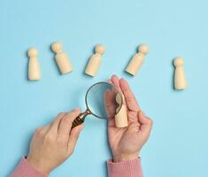 Wooden men and a magnifying glass on a blue background. Recruitment concept, search for talented and capable employees photo