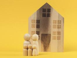 casa de madera y figuras en miniatura de una familia sobre un fondo amarillo. el concepto de venta y compra de bienes raíces foto