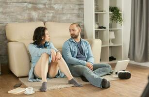 Couple looking at each other sitting down living room carpet. photo