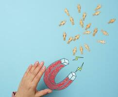 A woman's hand holds a drawn magnet, and figurines of people are drawn towards it, symbolizing the concept of recruiting and talent acquisition photo