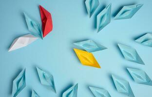 A group of paper ships against another aggressive group on a blue background. Association concept, top view photo
