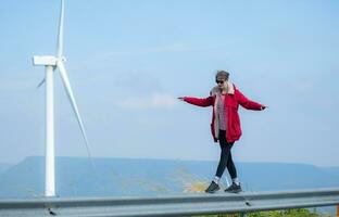 en el antecedentes de molinos de viento, un joven mujer en un rojo chaqueta es disfrutando su invierno vacaciones. foto