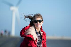 en el antecedentes de molinos de viento, un joven mujer en un rojo chaqueta es disfrutando su invierno vacaciones. foto