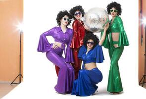 A group of girls in colorful costumes with a disco ball pose in the studio on a white background. photo