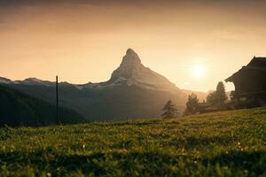 Sunset over Matterhorn mountain with wooden cottage on pasture in rural scene at Zermatt, Switzerland photo