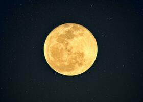 Yellow full moon with crater textured glowing with starry in night sky photo