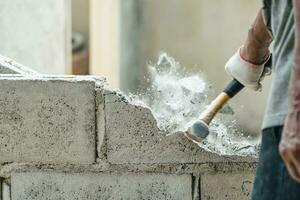 Hand of worker using hammer smashing and demolish on brick wall at construction site photo