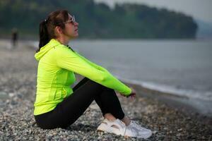 A woman is sitting on the beach in sportswear. photo