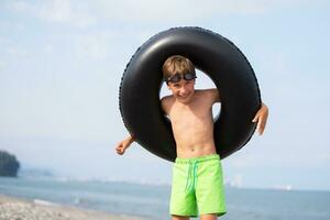 contento chico con nadando anillo y gafas de protección por el mar. foto