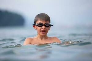 un chico en nadando gafas de protección nada en el mar. foto