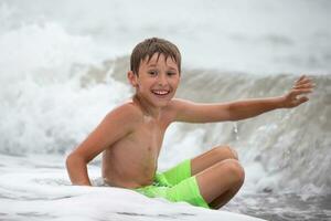 Happy boy in a sea wave bathing looks at the camera. photo