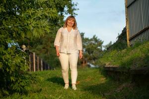 A beautiful blond woman with a full build walks in a green park. photo