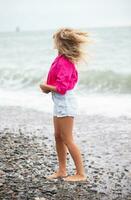 Beautiful woman on the background of the sea in denim shorts and a bright shirt. photo