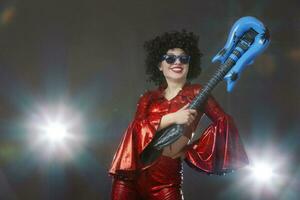 Funny pop singer with a toy guitar on a gray background. photo