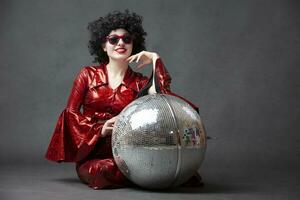 Disco style girl in a red shiny suit posing with a disco ball. photo