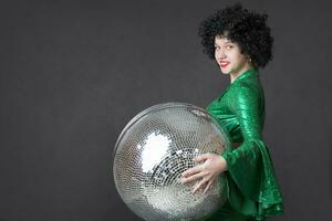 Beautiful girl holding a disco ball on a gray background. Disco style. photo