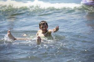 contento chico nada en el mar, obras de teatro con el ondas. niño en vacaciones a el playa. foto