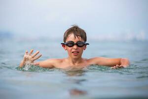 A boy in swimming goggles swims in the sea. photo