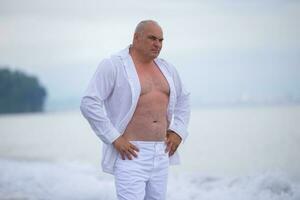 Handsome elderly man of athletic build in light clothes on the seashore. photo