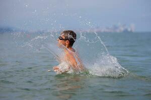 A boy in swimming goggles bathes in the sea, plays with the waves, runs and splashes water. photo