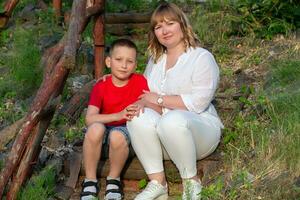 Happy mom and son on a summer walk sit on a wooden bench pose, look at the camera. photo