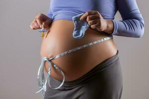imagen de estómago de embarazada mujer con un azul cinta participación chupete y calcetines para bebé chico en gris antecedentes. foto