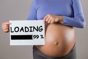 Image of close up stomach of pregnant woman holding paper with text loading on gray background. photo