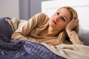 Sad woman in pajamas lying on a bed in bedroom. photo