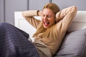 mujer teniendo fuerte dolor de cabeza mientras sentado en dormitorio. foto