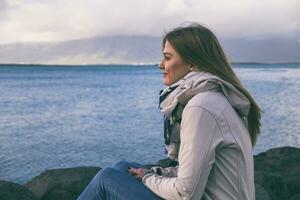 Beautiful woman enjoys sitting by the sea in Reykjavik.Image contains little noise because of high ISO set on camera and it is toned. photo