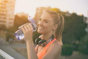 Beautiful sporty woman drinking water while resting from exercise.Toned image. photo