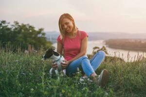 Beautiful woman enjoys spending time with her dog Jack Russell Terrier outdoor with a cityscape and river view behind her.Toned image. photo