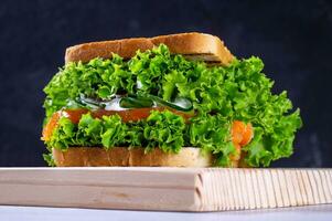 Sandwich with fresh salmon, lettuce, cucumber and sauce on a cutting board, on a dark background. Homemade. Healthy convenience food. photo