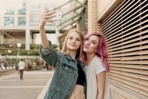 Two happy girlfriends taking photo with their smartphone in the city