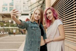 Two happy girlfriends taking photo with their smartphone in the city