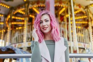 pink hair girl short haircut posing in amusement park on carousel background. photo