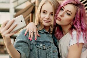 Two happy girlfriends taking photo with their smartphone in the city