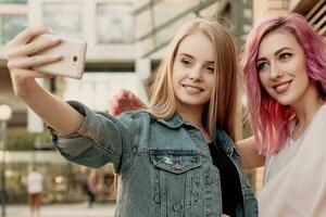 Two happy girlfriends taking photo with their smartphone in the city