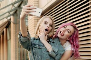 Two happy girlfriends taking photo with their smartphone in the city