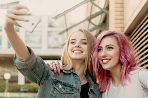 Two happy girlfriends taking photo with their smartphone in the city