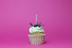 birthday cupcake with one burning candles over pink background photo